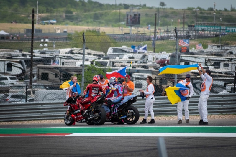 Motorcycle racers stopped on track as marshals wave national flags after the race