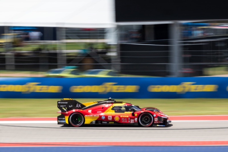 A red and yellow Ferrari 499P Le Mans Hypercar at speed past Goodyear signage