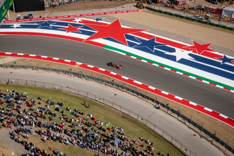 A McLaren Formula 1 car rounding a star-painted corner as spectators watch from a grassy bank at the Circuit of the Americas