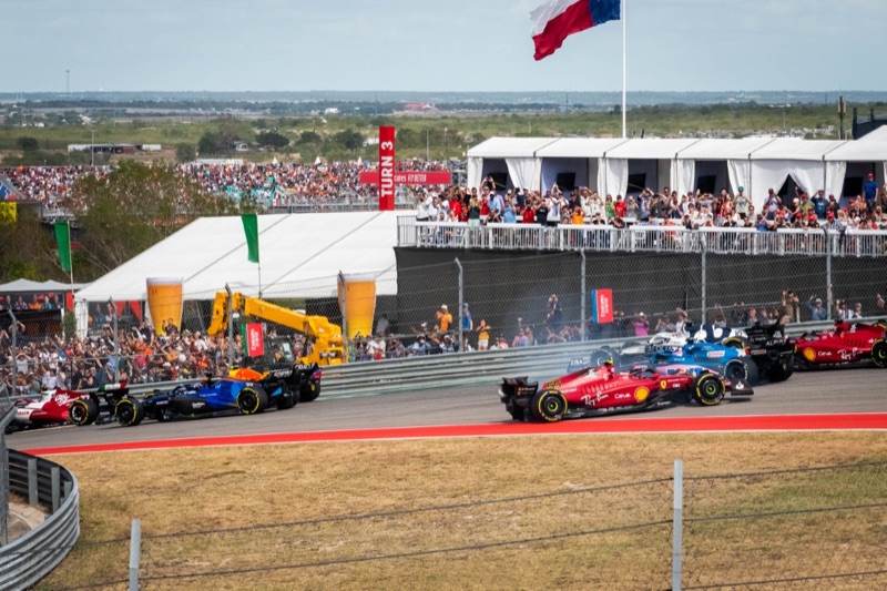 Carlos Sainz in his red Ferrari faces the wrong way at the top of Turn 1 as the rest of the field drives by and packed grandstands look on